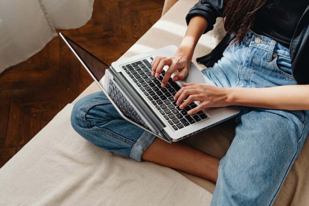 Close-up of a woman typing on a laptop, sitting cross-legged indoors.
